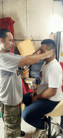 a man is cutting another man 's hair with a razor