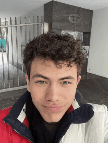 a young man with curly hair stands in front of a building with a sign on it that says a + a