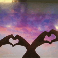 a person making a heart shape with their hands in front of a purple sky