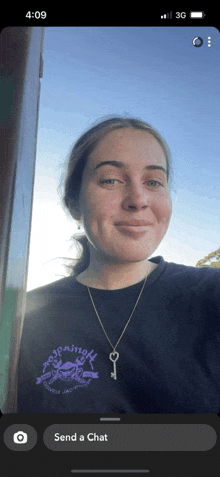 a woman wearing a purple shirt and a key necklace is taking a selfie on a phone