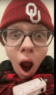 a young boy wearing glasses and a red beanie with the letter u on it