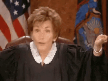 a female judge is sitting in front of an american flag and making a funny face .