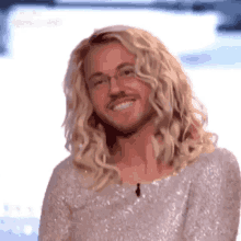 a man with long blonde hair and a beard is smiling while wearing a sequined dress .