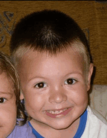 a young boy with a shaved head is smiling next to a little girl