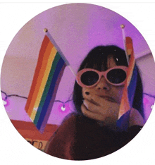 a girl wearing sunglasses holds a rainbow flag