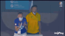 a man wearing a mask is standing next to another man wearing a yellow shirt .