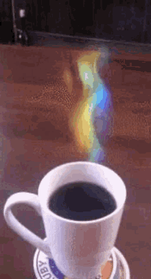 a cup of coffee is on a coaster on a table with a rainbow coming out of it .