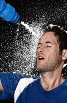 a man in a blue shirt is spraying water on his face