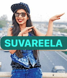 a woman wearing sunglasses and a hat stands in front of a sign that says suvareela