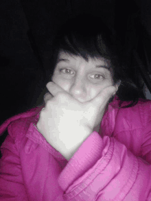 a woman in a pink jacket covers her mouth with her hand