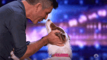 a man is petting a brown and white dog on a stage with a nbc logo in the background .