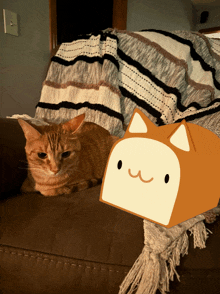 a cat laying on a couch next to a box with a face on it