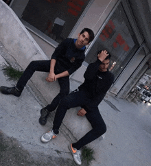 two young men are sitting on a sidewalk in front of a building with a sign that says ' a.m. '