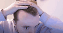 a man is touching his hair with his hands while wearing a blue shirt .