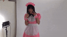 a woman in a pink maid costume is standing in front of a white wall in a room .