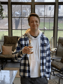 a man in a plaid shirt holds up a bottle of corona