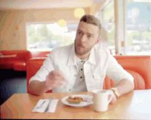 a man in a white jacket sits at a diner table with a plate of food and a cup of coffee