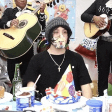 a man sitting at a table with his face covered in cake and a birthday hat