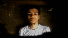 a man in a white shirt looks at the camera with a dark background