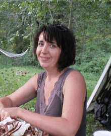 a woman in a gray tank top is smiling while sitting outside