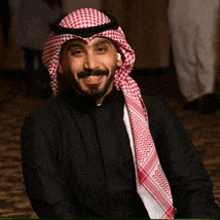 a man wearing a black shirt and a red and white head scarf smiles