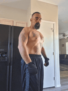 a shirtless man with a tattoo on his chest is standing in front of a black refrigerator