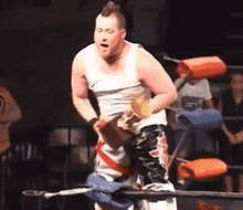 a man in a white tank top is standing in a boxing ring holding a belt .