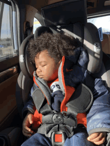 a young boy sleeping in a car seat with a nike jacket