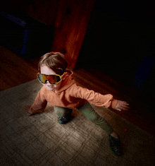 a young boy wearing sunglasses is crawling on the floor with his arms outstretched