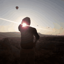 a man stands in front of a sunset with hot air balloons flying in the sky