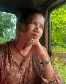 a woman wearing a watch and a red necklace looks out the window