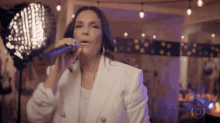 a woman in a white jacket is singing into a microphone in a room