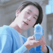 a young man in a blue sweater is holding a blue and white water gun .