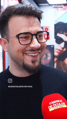 a man wearing glasses is smiling in front of a microphone that says fabrica de oculos