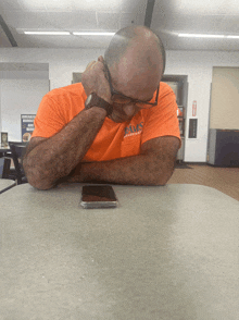 a man sitting at a table wearing an orange shirt that says alms