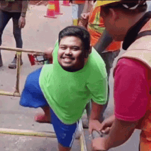 a man in a green shirt and blue shorts is smiling while standing next to another man in an orange vest