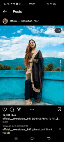 a woman in a black and gold dress is standing on a blue wall with mountains in the background