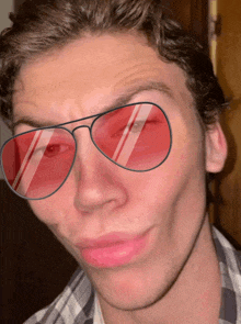 a man wearing a plaid shirt and red sunglasses is making a funny face