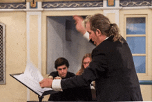 a man in a black suit stands in front of a podium with sheet music on it