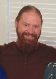 a man with a beard and a brown shirt smiles for the camera