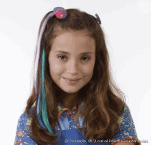 a young girl with long brown hair and blue and purple hair extensions is smiling for the camera .