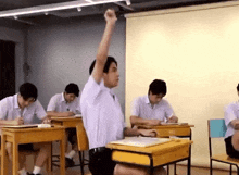 a group of students are sitting at their desks in a classroom raising their hands to answer a question .