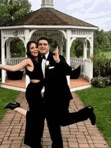 a man in a tuxedo and a woman in a black dress are posing in front of a gazebo .