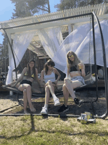 three girls are sitting on a swing and one is drinking