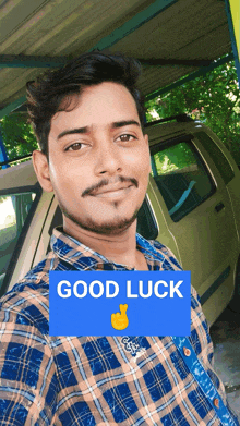 a man in a plaid shirt is standing in front of a car and a sign that says good luck