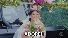 a bride in a wedding dress is holding a bouquet of flowers and smiling while standing next to a car .