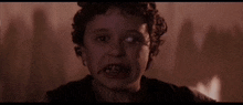 a close up of a child with blood on his face in a dark room with a fire in the background .