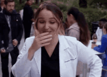 a woman in a lab coat is covering her mouth with her hand while standing in front of a crowd .