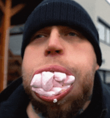 a man with marshmallows in his mouth wearing a black beanie