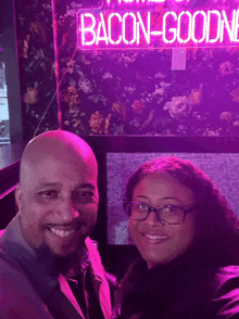 a man and woman are posing in front of a sign that says bacon-goodne